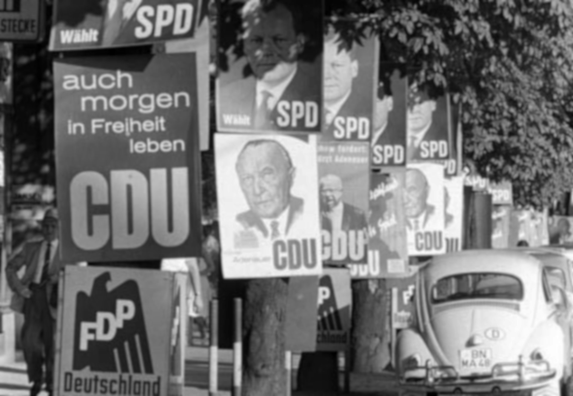 Schwarz-Weiß-Fotografie: an Bäumen befestigte Wahlplakate der FDP, CDU und SPD.
