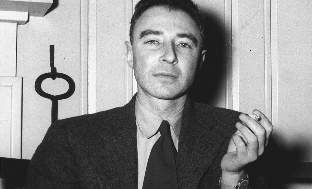 Schwarz-Weiß-Porträt von J. Robert Oppenheimer im Sakko mit Krawawtte, seine linke Hand hält eine Zigarette.